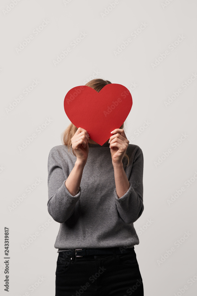 young woman hiding face behind empty red paper cut heart card isolated on grey young woman hiding face behind empty red paper cut heart card isolated on grey