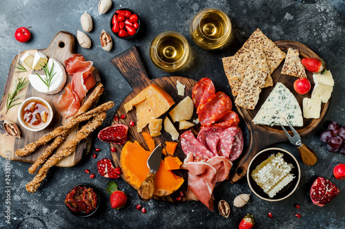 Appetizers table with italian antipasti snacks and wine in glasses. Brushetta or authentic traditional spanish tapas set, cheese variety board over black stone background. Top view, flat lay
