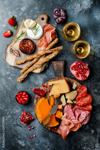 Appetizers table with italian antipasti snacks and wine in glasses. Brushetta or authentic traditional spanish tapas set, cheese variety board over black stone background. Top view, flat lay