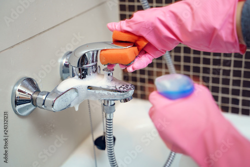 Woman 's hand in rubber gloves washing bathtub mixer