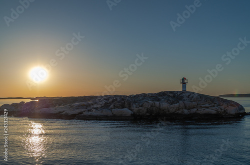 Lighthouse on an islet at sea in front of a sunset reflecting in the water