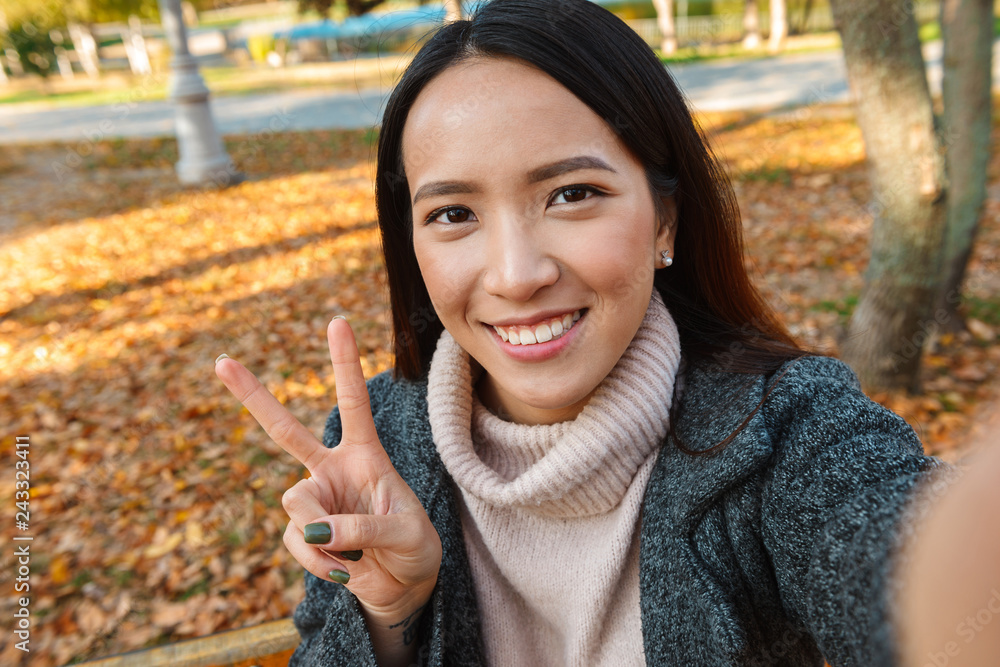 Smiling young asian woman wearing coat sitting on a bench Smiling young asian woman wearing coat sitting on a bench