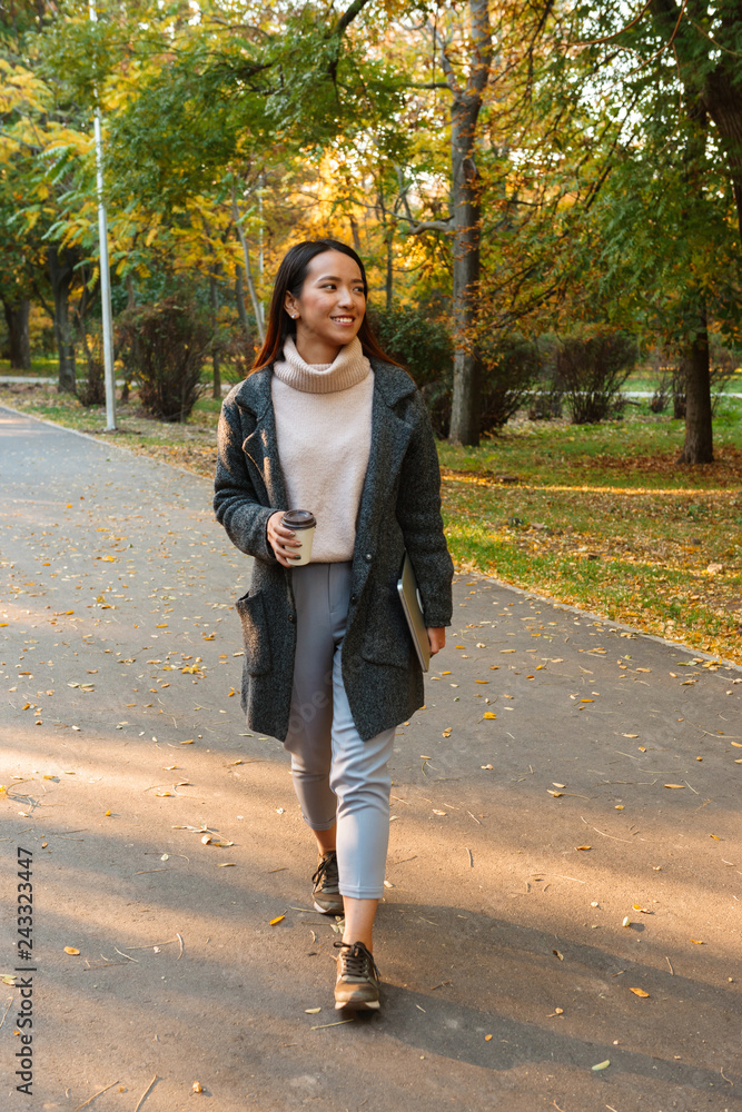Fototapeta premium Smiling young asian woman wearing coat walking