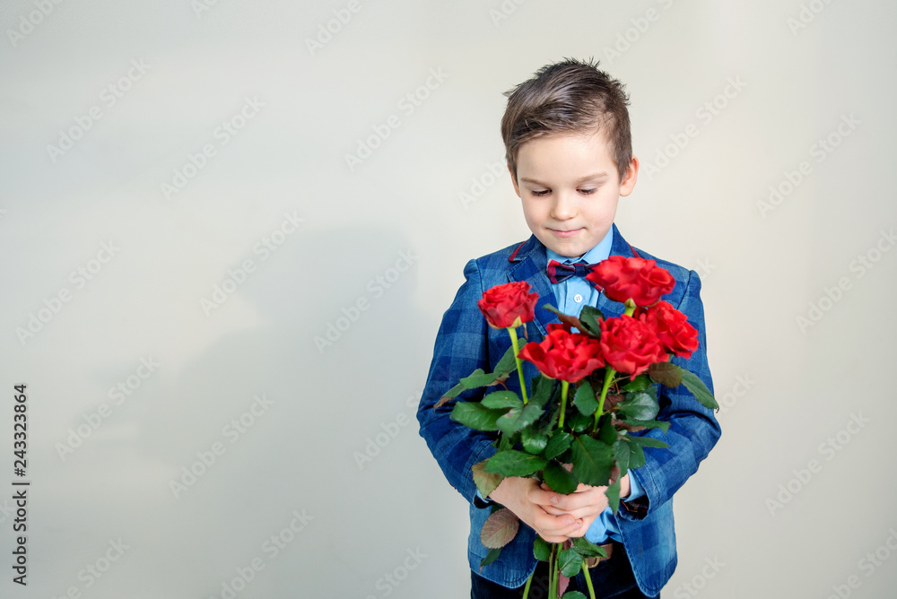 Adorable little boy in suit with bouquet of red roses on a light background Adorable little boy in suit with bouquet of red roses on a light background