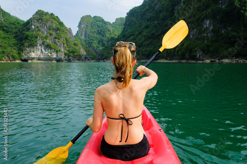 Woman on kayak paddling through karst islands and dense jungle in Halong Bay / Cat Ba island areas in Vietnam.