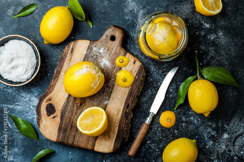 Preserved, salted canned lemons on a wooden board over black stone background. Moroccan cuisine