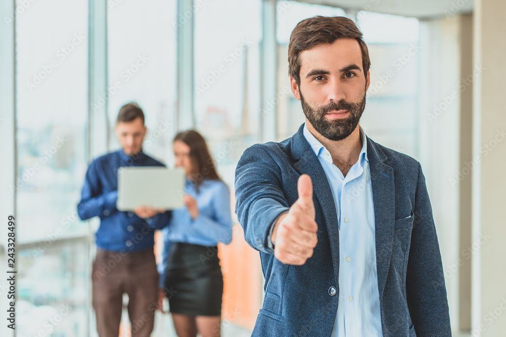 A businessman stands in the office showing a hand gesture of a class. During this time, he stands against the background A businessman stands in the office showing a hand gesture of a class. During this time, he stands against the background