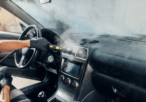 Carwash, worker cleans salon with steam cleaner photo