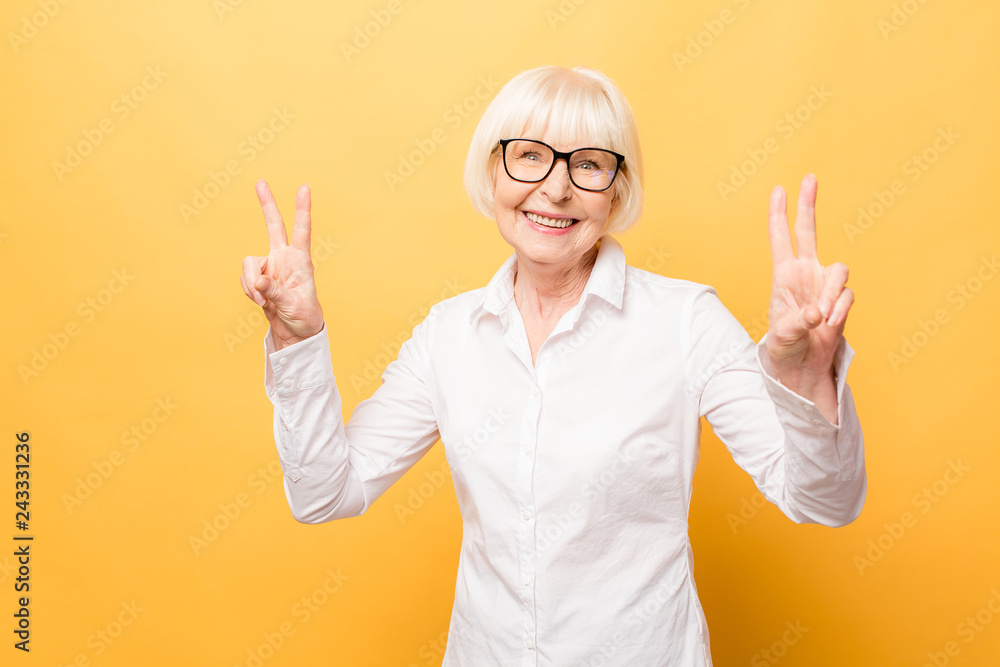 Portrait of a cheerful senior woman gesturing victory isolated over yellow background. Portrait of a cheerful senior woman gesturing victory isolated over yellow background.