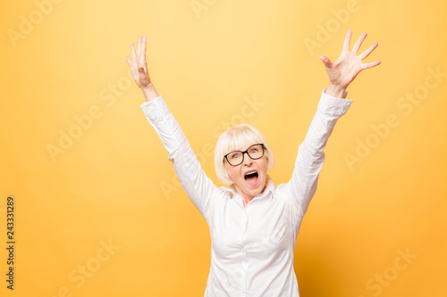 I'm winner! Portrait of a cheerful senior woman gesturing victory isolated over yellow background.