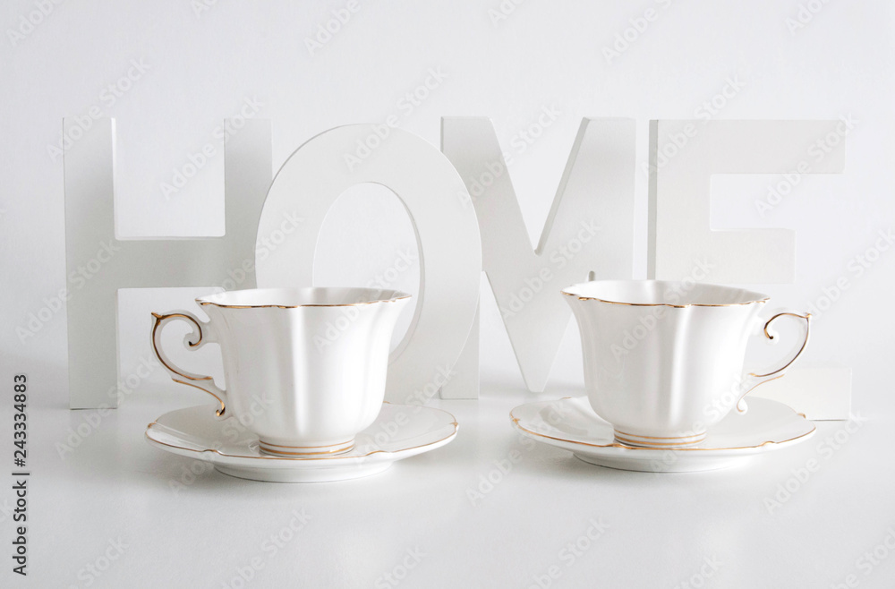 White letters, word home and two elegant white cups on white background. Home decor
