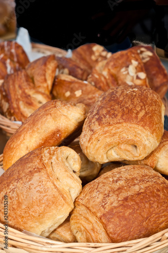  Front view, close up of a group of freshly baked, homemade, artisan, golden, almond croissants in a wood, wicker baket, on display and for sale at a tropical farmers market