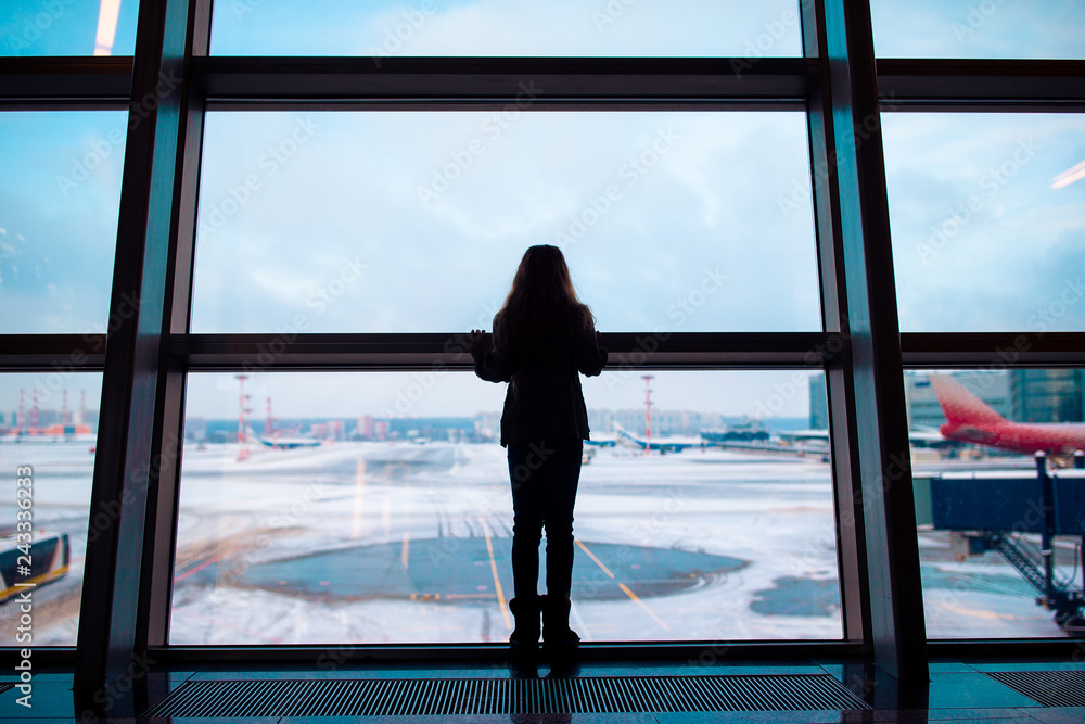 Fototapeta premium Little girl in airport near big window while wait for boarding