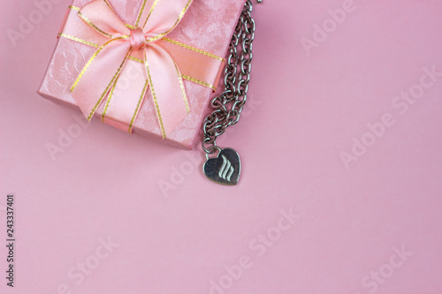 A gift in a beautiful box and a necklace with a heart on a pink background. Valentine's Day, International Women's Day.