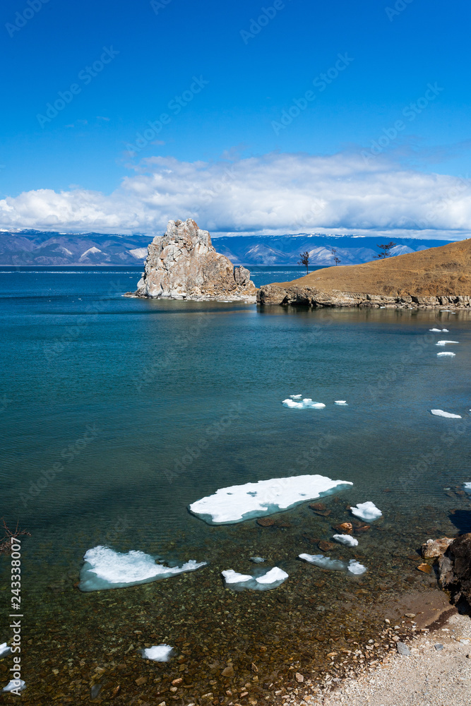Baikal Lake in the spring sunny day. Melting ice floes near the shore of Olkhon Island. View on the natural landmark - Shamanka Rock