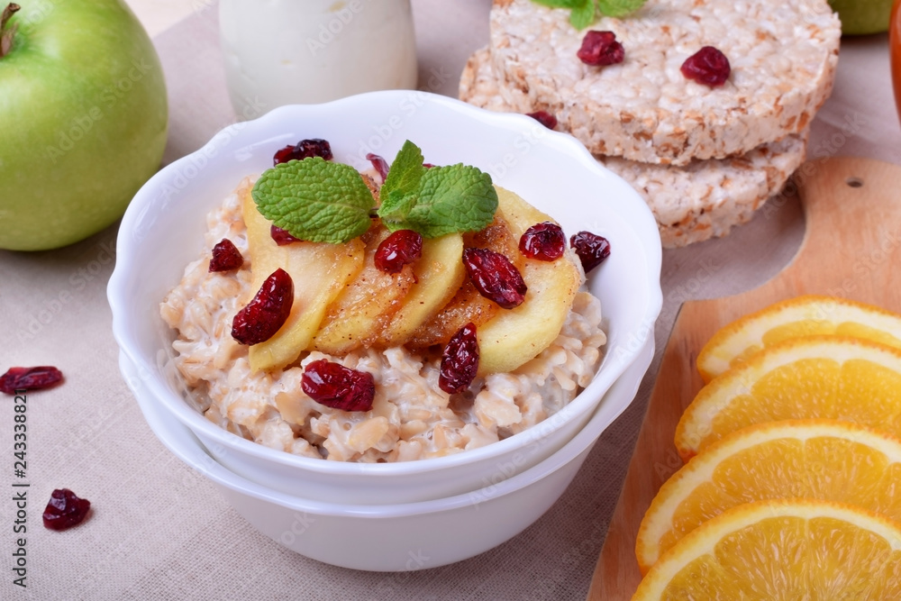 Porridge with caramelized apples and dried cranberries topped with mint surrounded by breakfast ingredients Porridge with caramelized apples and dried cranberries topped with mint surrounded by breakfast ingredients