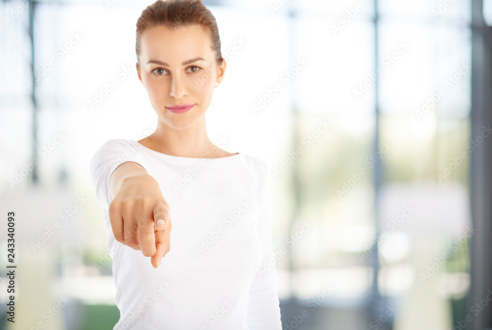 Close-up shot of a young woman smiling and pointing at you while standing at the office. Close-up shot of a young woman smiling and pointing at you while standing at the office.