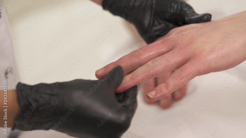 A close-up of woman's hands in black gloves massaging man's left hand, palm and fingers in a beauty salon A close-up of woman's hands in black gloves massaging man's left hand, palm and fingers in a beauty salon