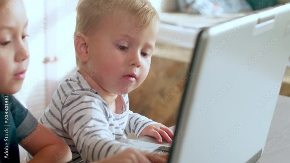 Cute little boy and girl using touchscreen of modern laptop and having fun together at kitchen table Cute little boy and girl using touchscreen of modern laptop and having fun together at kitchen table