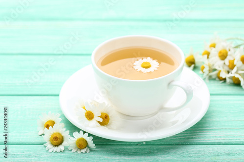 Cup of tea with chamomile flowers on mint wooden table