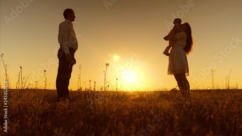 Little daughter goes to her mother in her arms at sunset. Happy mother hugs and kisses baby. Dad  mom and baby are playing for walk in evening. First steps.