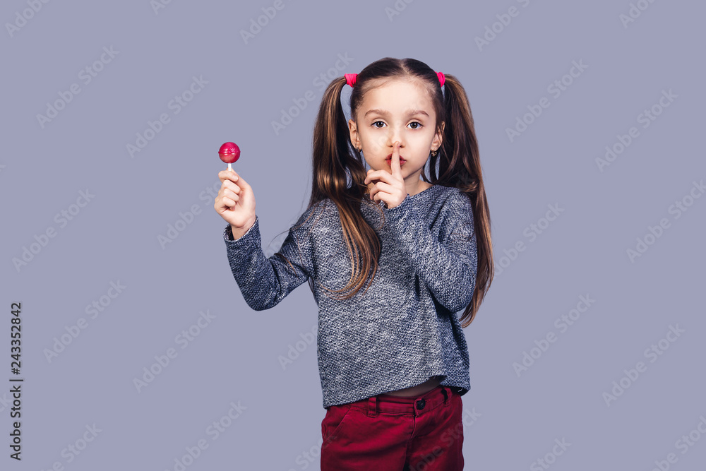 little cute girl holds red lollipop in hand and shows shh. little cute girl holds red lollipop in hand and shows shh.