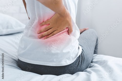 Woman suffering from back pain, sitting on bed photo