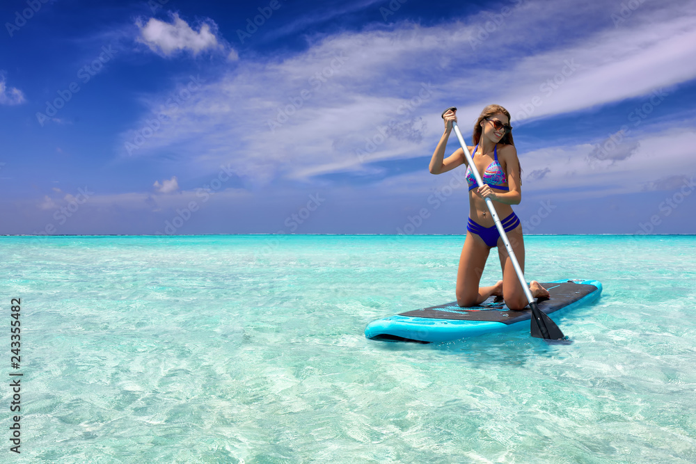 Sportliche Frau im Bikini auf einem SUP Board auf tropischen, türkisen Gewässern