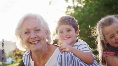 Portrait Of Smiling Grandparents Carrying Grandchildren Outdoors In Summer Park photo