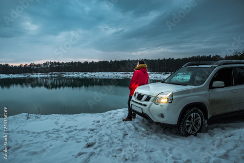 man near suv car at winter time. lake with forest on background