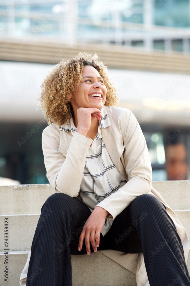 young african american woman sitting on steps in city and laughing