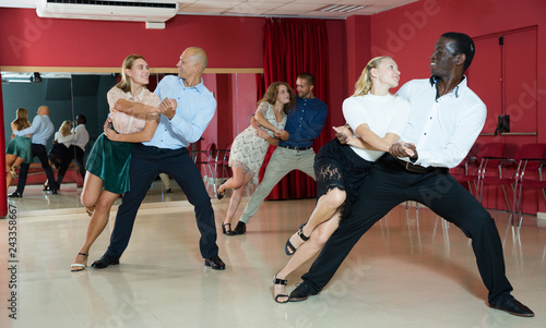 Portrait of positive adult pairs enjoying tango in modern dance hall