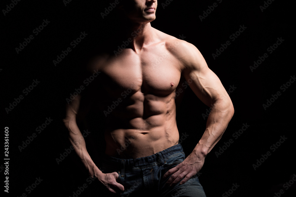 Fototapeta premium Fitness concept. Muscular and fit torso of young man having perfect abs, bicep and chest. Male hunk with athletic body on black background