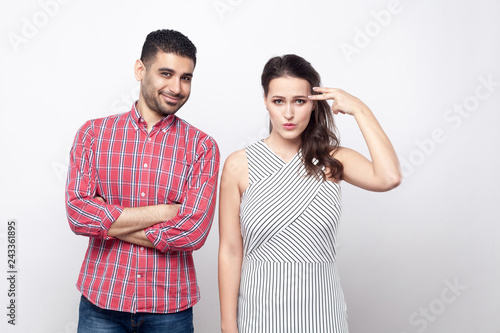 Portrait of funny smiley handsome man in red checkered shirt and crazy tiredwoman in white striped dress with pistol gesture standing and looking at camera. photo