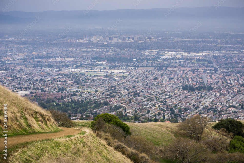 Aerial view of residential areas of San Jose, California on a rainy day; hiking trail in Sierra Vista park on the right; the city's financial district in the background;
