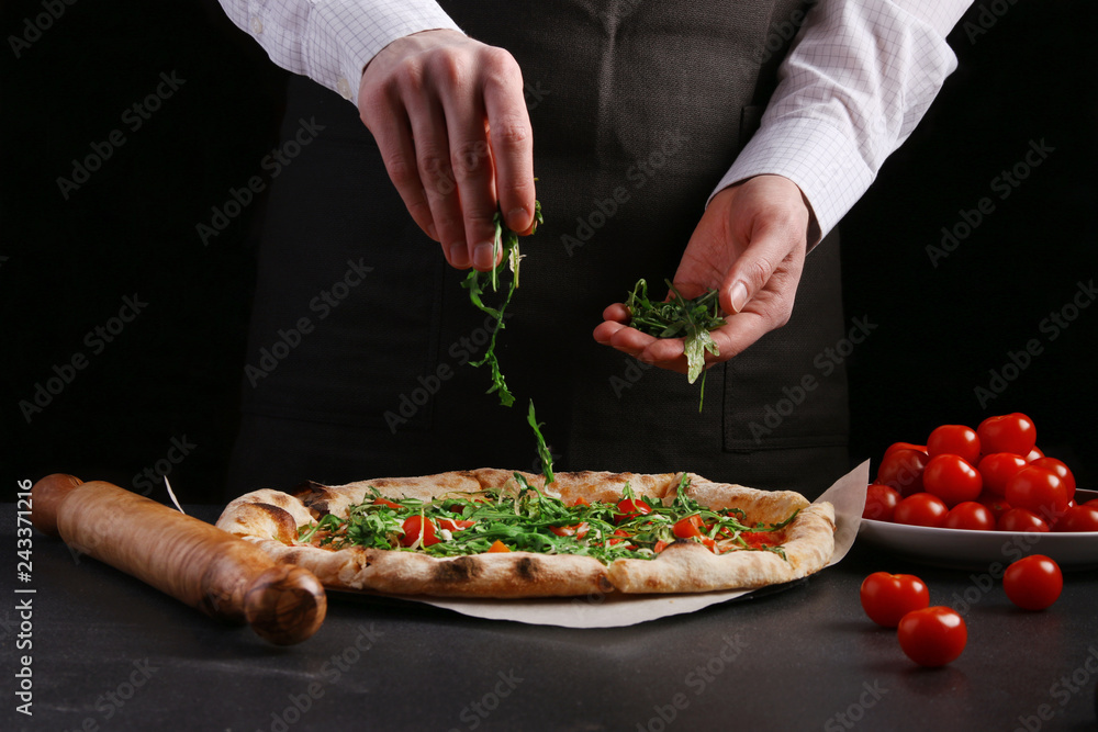 The chef in black apron makes pizza with vegetables