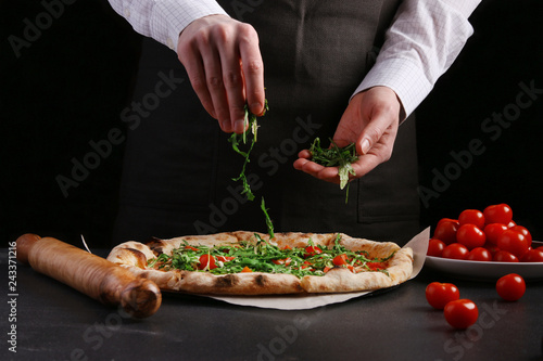Fototapeta Naklejka Na Ścianę i Meble -  The chef in black apron makes pizza with vegetables