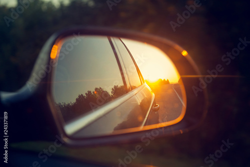 the sunset is reflected in the rear mirror of the car