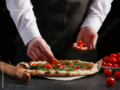 Chef puts cherry tomatoes in pizza preparation of traditional Italian pizza. cooking pizza concept. pizza making on black background