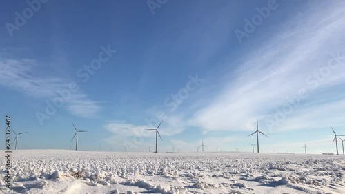 Wind energy farm in snowy field in ND with propellers spinning from wind together on beautiful sunny day.