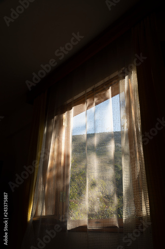 In sunny morning, from window of a room, romantic mountain view behind the curtains