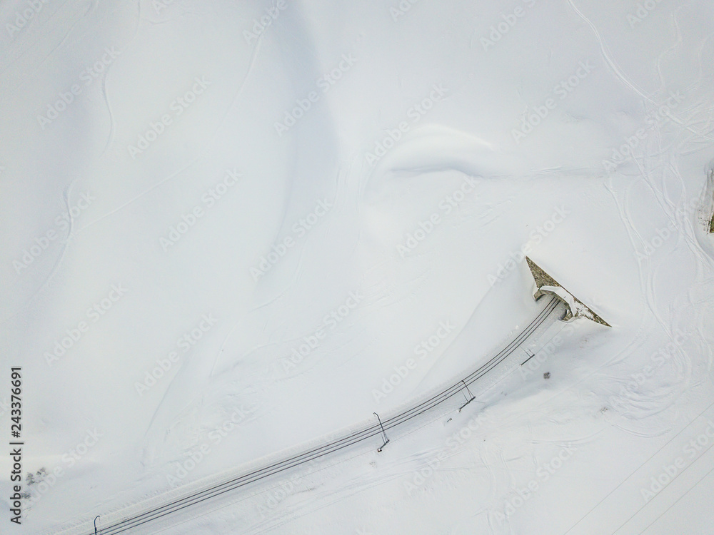 Aerial view of tunnel entrance in snow covered landscape. Railroad track going in tunnel in swiss alps.