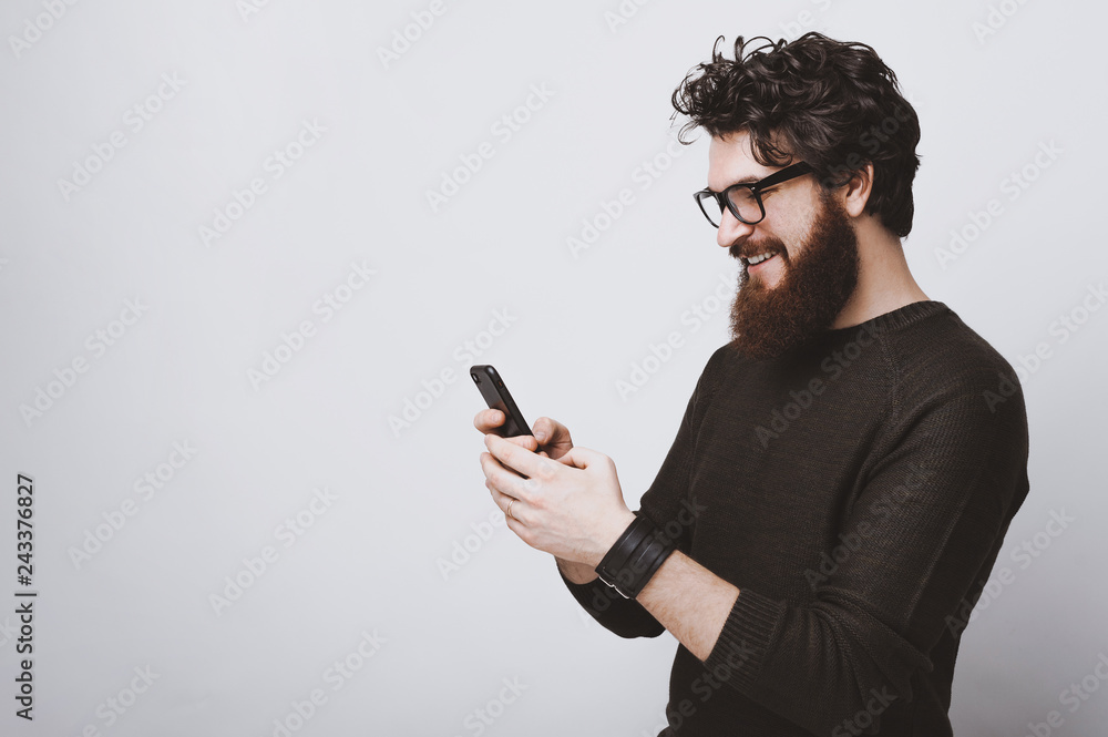 Handsome bearded model is posing with phone in hands over white background Handsome bearded model is posing with phone in hands over white background