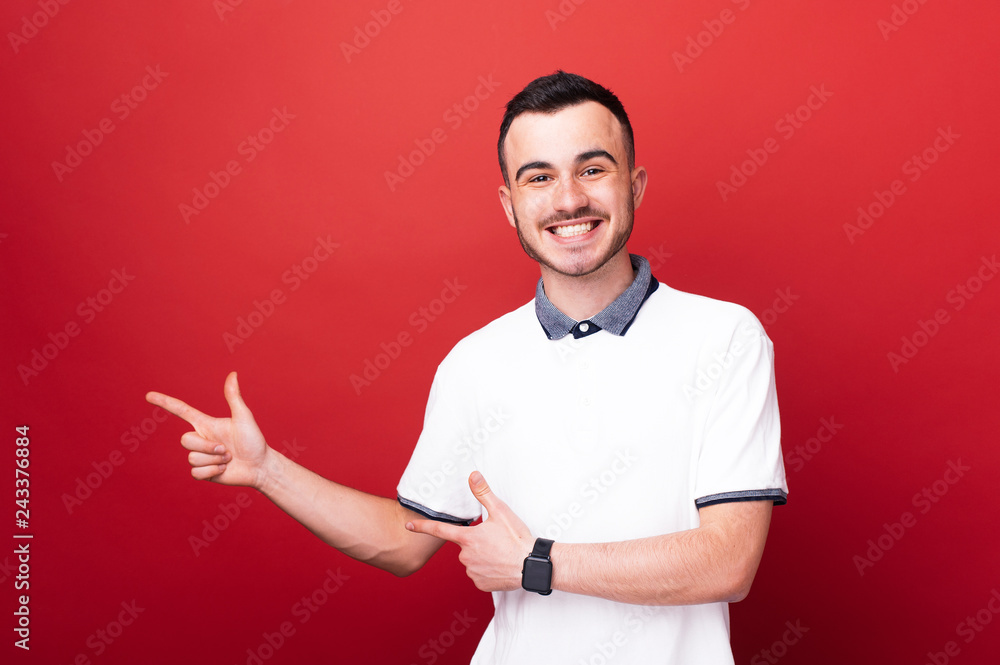 Happy smiling boy is pointing left at copy space over red background Happy smiling boy is pointing left at copy space over red background