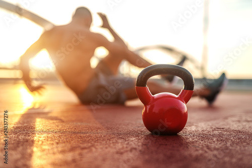 Fototapeta Naklejka Na Ścianę i Meble -  Silhouette of shirtless man doing crunches in the court in the morning. Selective focus on kettlebell.