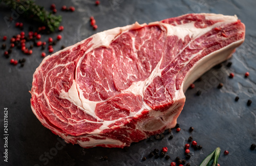 raw cowboy steak with seasonings on stone background, prime rib eye on bone photo