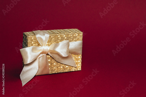Golden present box with a silk bow on deep red background. Copy space. photo