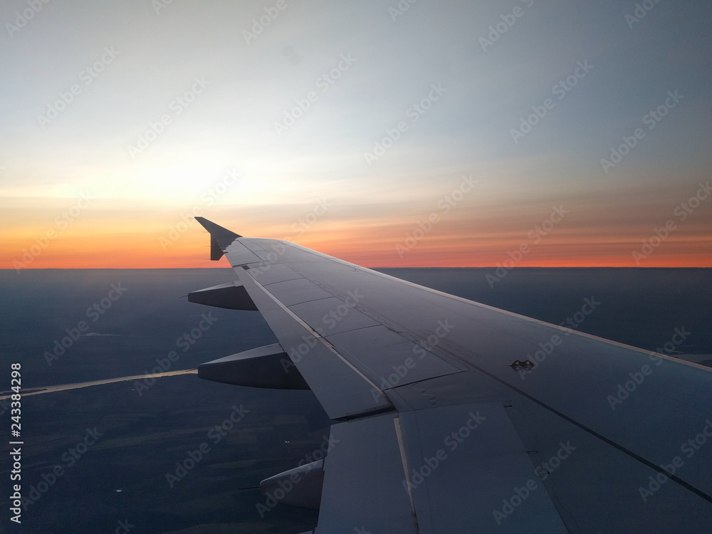 View from airplane window to beautiful sunrise or sunset. Wing of plane flying above in the sky.