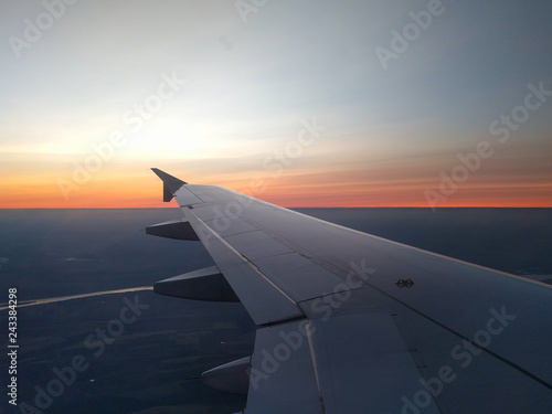 View from airplane window to beautiful sunrise or sunset. Wing of plane flying above in the sky.