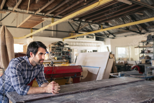 Woodworker leaning on a workshop bench deep in thought